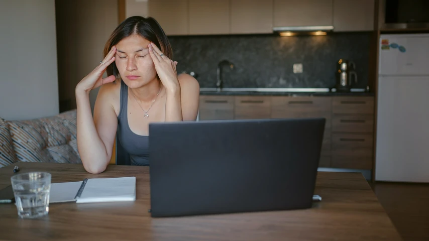 Woman Sitting in Front of Laptop While Rubbing her Temples